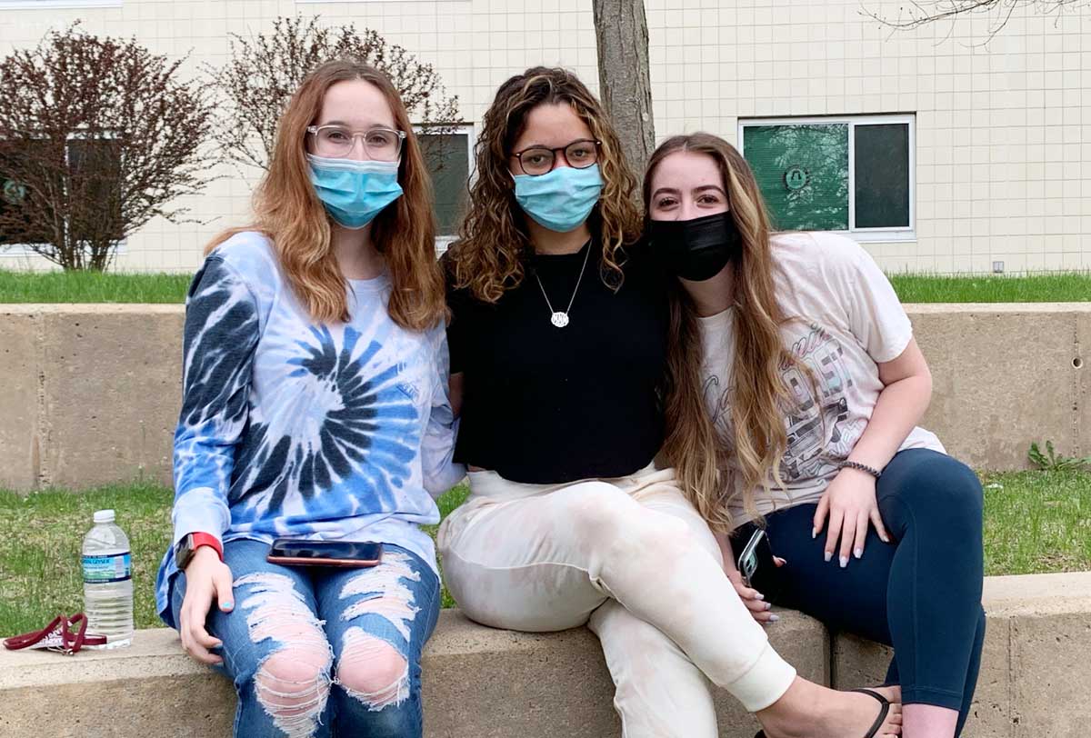 Three female students sitting outside together wearing masks