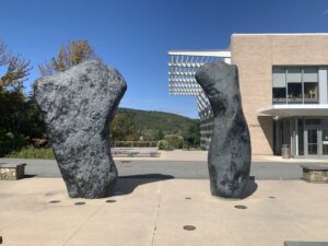 Image of an outdoor sculpture comprised of what appear to be two large boulders. The rock formations are actually bronzes, and look vaguely like human torsos with no head or limbs.