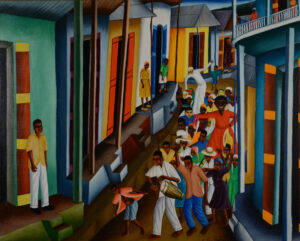 Brightly colored houses line a dirt road. On the porches of these houses stand a few individuals, watching as a crowd parades down the street.The crowd is comprised of many people, those in front carrying drums and wind instruments. In the back, some figures wear masks. There are two very tall figures, likely puppets or people on stilts. Closer to the front is a black woman in a red dress with gold hoop earrings. In the back is an extremely tall white figure with a skeleton face.