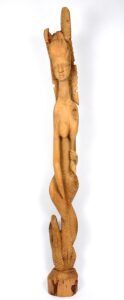 A tall wood carving of a mermaid. The woman pulls on her left breast with her left hand, elongating it toward her tail. Her right hand ends without a hand, and her tail flips back up on itself at the end.