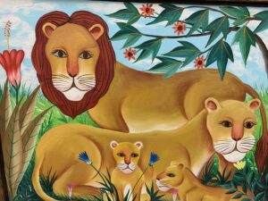 A family of four lions- a male, a female, and two cubs. The male stands while the female and cubs rest. 