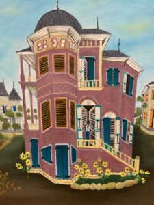 A pink, three-story victorian-style house with blue and orange shutters and pale-yellow stairs. On the second floor landing, a man stands in the doorway, french doors open behind him. There are small yellow flowers in a garden in front of the house, and the rest of the foreground is dirt. Two other houses, white, are in the distance on either side of the pink house.