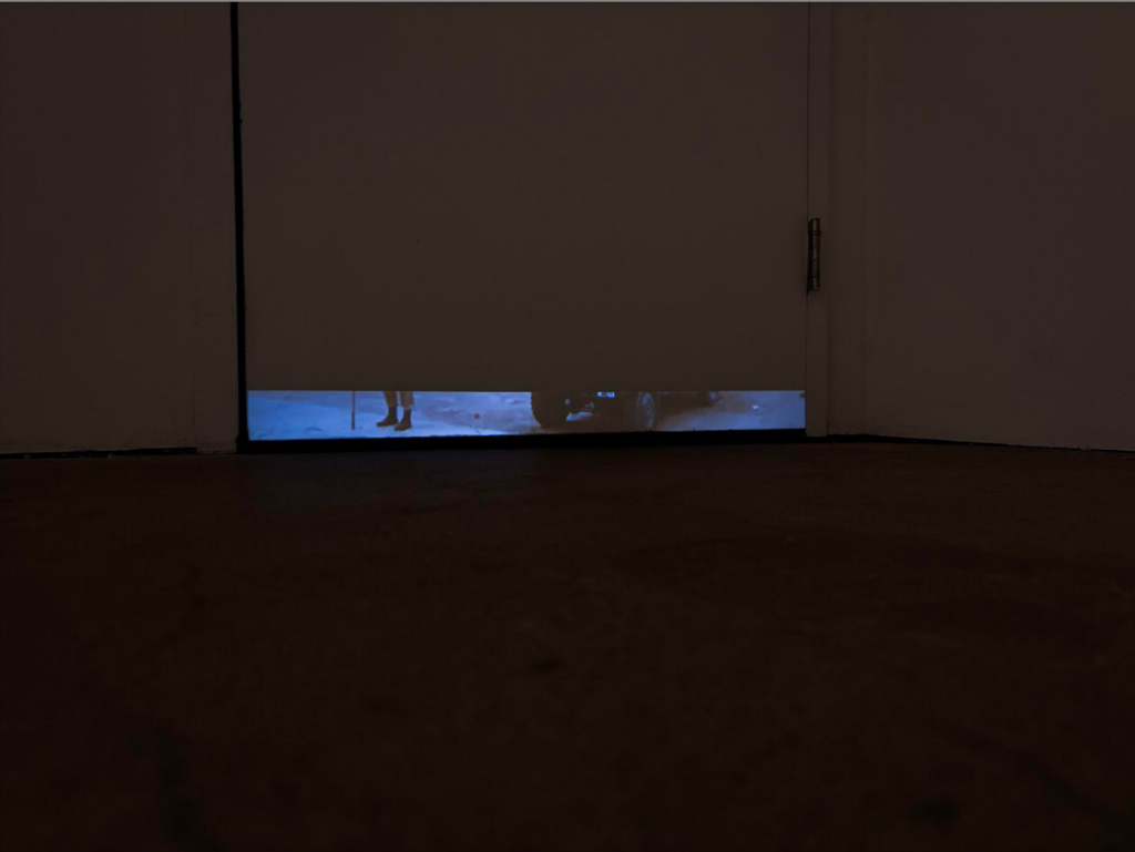 A dark room with a narrow projection, close to the ground, of someone's feet.