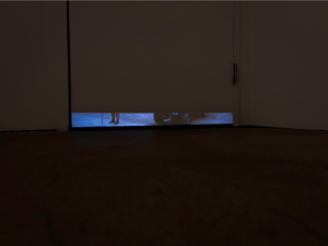 A dark room with a narrow projection, close to the ground, of someone's feet.