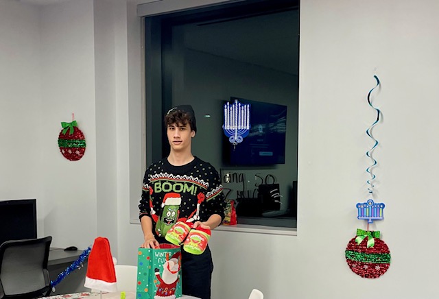 Evan opening his Kermit-the- Frog slippers, Ugly Sweater Holiday Party 2023