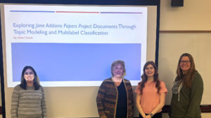 Four people in front of a projected slide "Exploring Jane Addams Documents through Topic Modeling and Multilable Classification