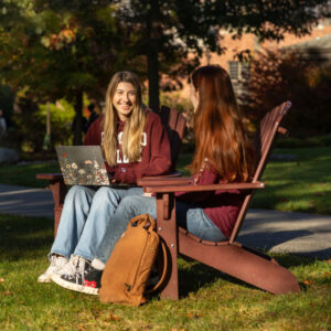 Two students sitting on Adirondack chairs wearing Ramapo College maroon sweatshirts