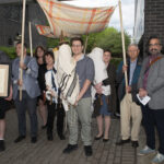 Students and dignitaries standing outside on Ramapo campus, holding three Torahs and a framed certificate.