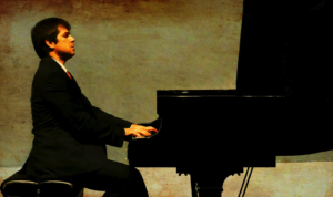 Itay Goren wearing a black suit and playing a black piano.