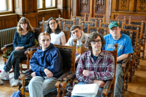 Students sitting in wooden chairs listening to a lecture.