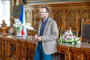 Picture of a white man in a blazer standing in front of a wooden dais.