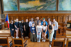 Wood paneled room with large frescos. Ten students, Dr. Labendz, and the Mayor of Kolín pose together.