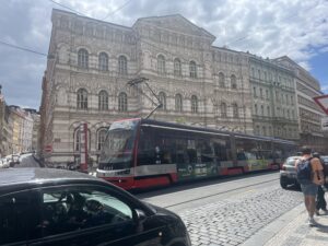 A white and red roundo-cubist building with a red and gray tram in front of it.