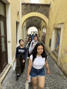 Students walking through a narrow yellow alleyway, under arcades.