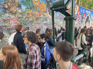 Students and tourists crowded in front of a graffitied wall, next to a green water pump.