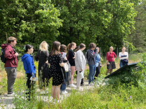Students standing at a large plaque installed in a field with trees in the background