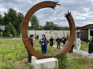 Students visible through a circular metal sculpture in a green field.