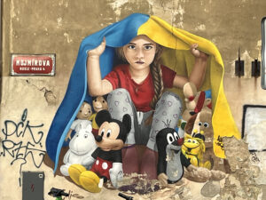 Pro-Ukrainian graffiti. A young girl with braided hair sits and covers herself and various cartoon characters with the Ukrainian flag.