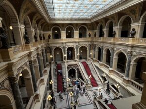 Large hall with two balcony levels with arches. Red carpets run down two stairways in the back