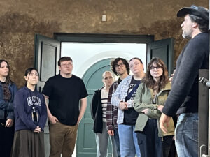 Students gathered in front of a door, speaking with a white man in a black hat.