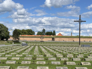 Military-style cemetery with a large cross in the distance, in front of an early modern fort.