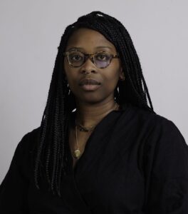 Headshot of Zoe Samudzi wearing a black shirt and glasses.