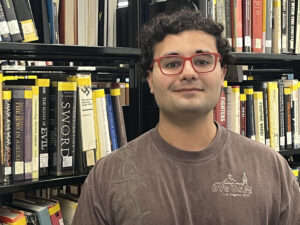 Headshot of James in front of library stacks.