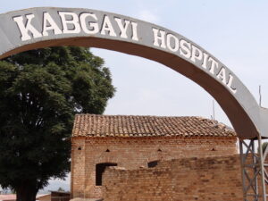 Arched gate with the words, "Kabgayi Hospital" written on it, in front of a brok building that looks damagaed.