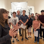 Students standing in an art gallery listening to a speaker.
