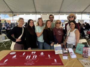 Director David Gurney is pictured smiling with 7 Ramapo Volunteers behind a table. The table has books, pamphlets, and DNA test materials used in the Ramapo College Latin American DNA Project.