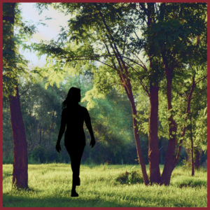 Silhouette of a woman walking through the woods as sunbeams break through the trees