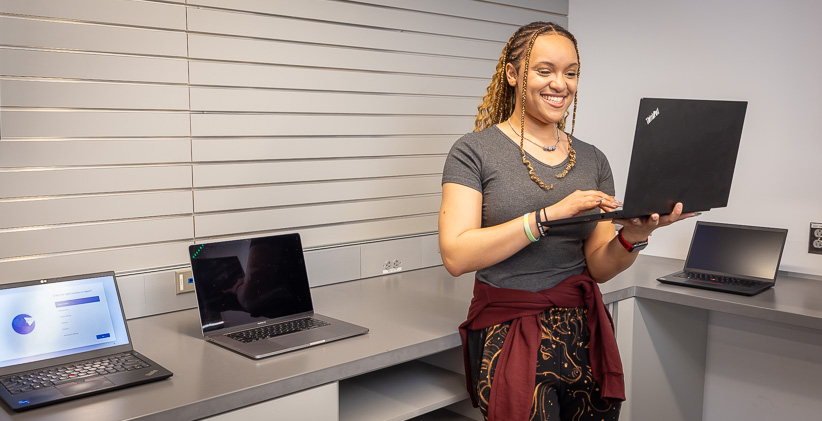 Student in a computer store, holding a laptop.
