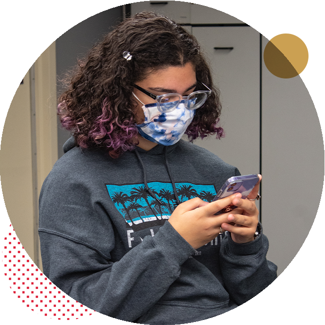 Student inside with mask on looks at phone