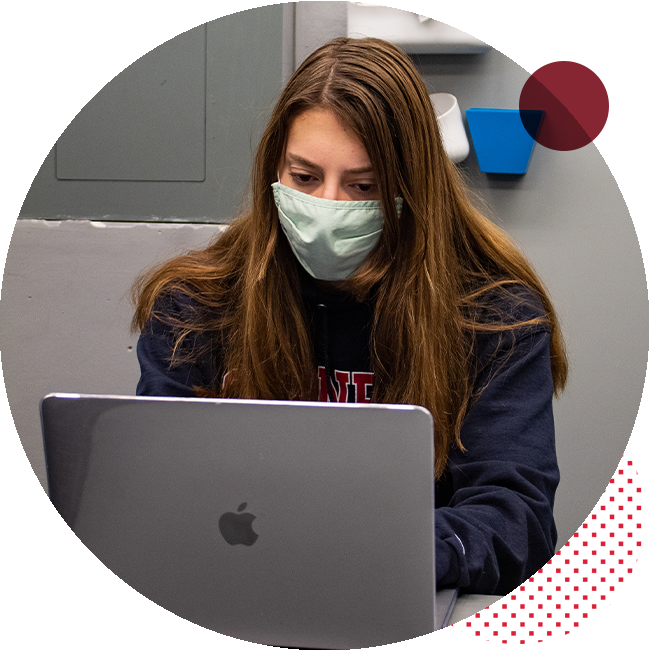 Student with mask on sits at a desk on a laptop