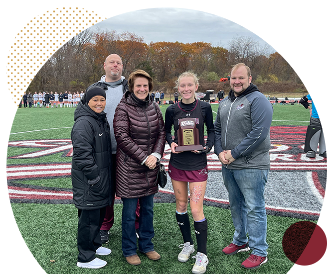 field hockey player holds MVP award surrounded by supporters