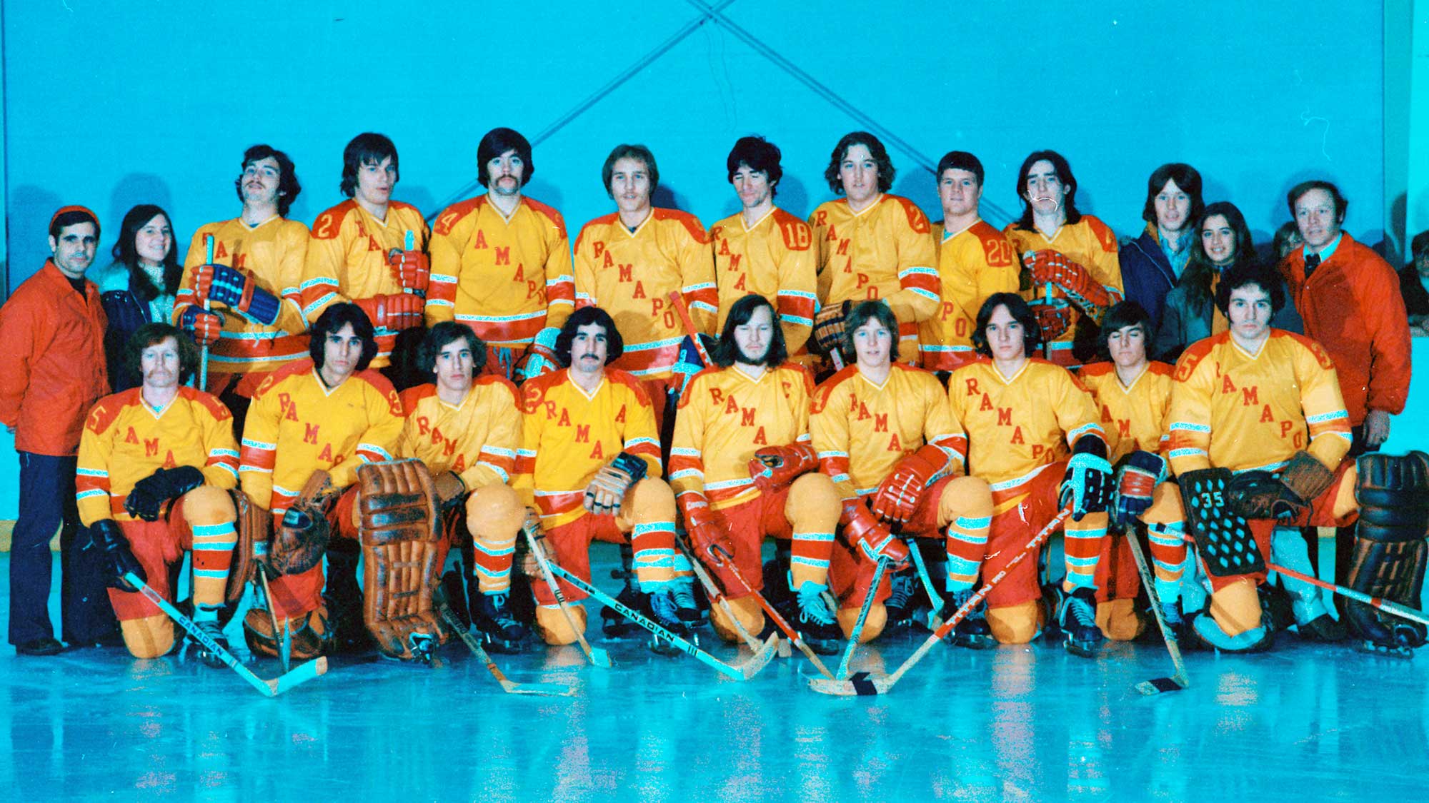1975 Ice Hockey group standing on the ice, wearing yellow and red uniforms