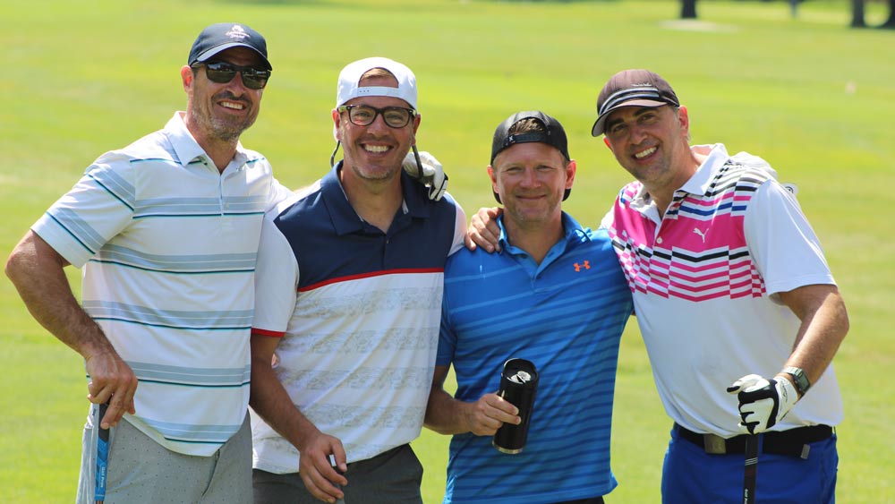 Four men standing together on the green for the Inaugural Golf Outing