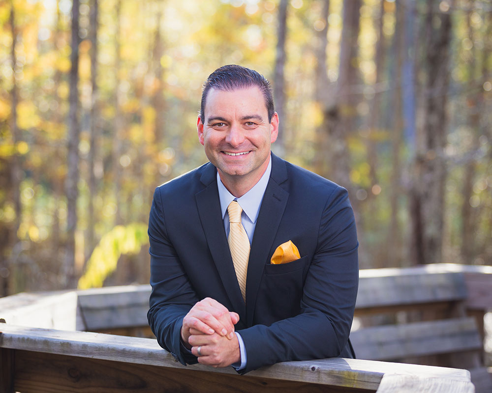 Bryan Steros smiling outside wearing a suit with a yellow tie