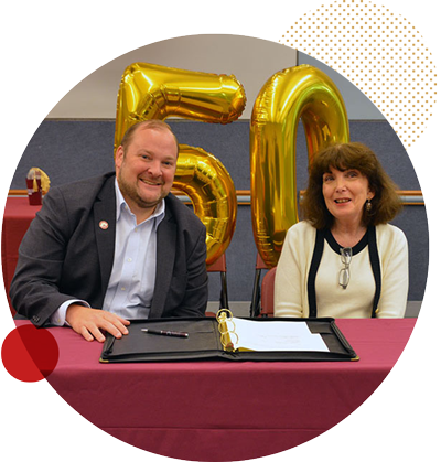 Chris Romano and Robin Keller sitting at a table with a 50th balloon behind them