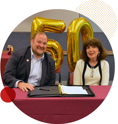 Chris Romano and Robin Keller Chris Romano and Robin Keller sitting at a table with a 50th balloon behind them