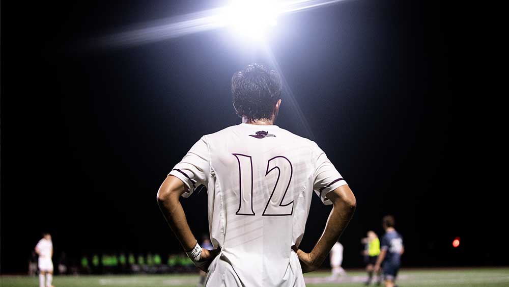 RCNJ soccer player with a bright light shining on him at night