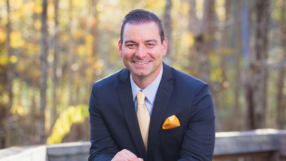 Bryan Steros smiling outside wearing a suit with a yellow tie