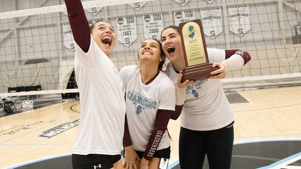 RCNJ Women's Volleyball players excitedly holding a trophy