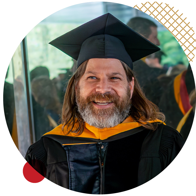 Assistant Professor Ken McMurdy wearing regalia outside of a building window.