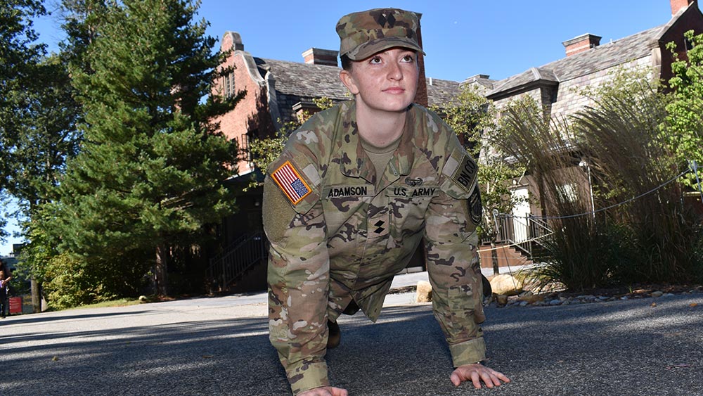 Balancing-Books-and-Battle-Drills_fall2025-home Olivia Adamson wearing her army uniform doing pushups outside in front of Ramapo College's mansion building