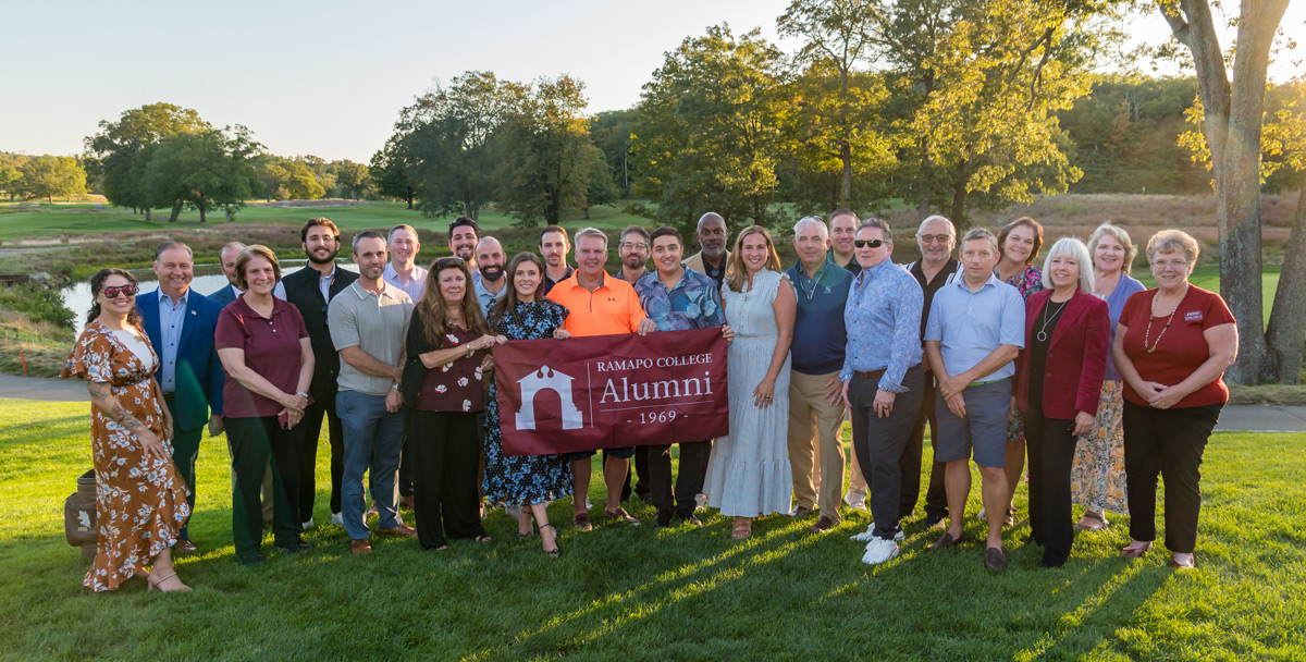 Ramapo College 2025 Golf Outing with a large group of people outside holding a Ramapo banner