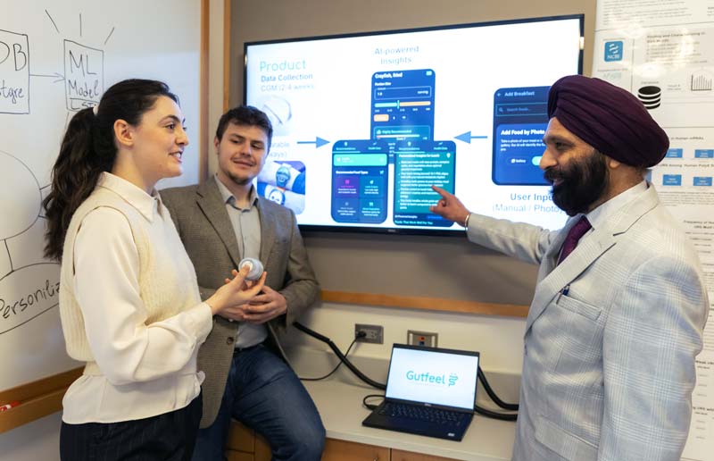 Paramjeet Bagga with two Ramapo College students discuss a product shown on a screen in an office. 