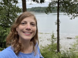 Dr. Natalie Lemanski standing among trees in front of a lake.