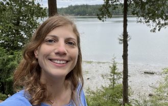 Dr. Natalie Lemanski standing among trees in front of a lake.