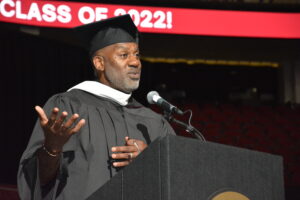 Keith Dawkins '94 in a cap and gown at the podium addressing the Class of 2022 at the Ramapo College Commencement